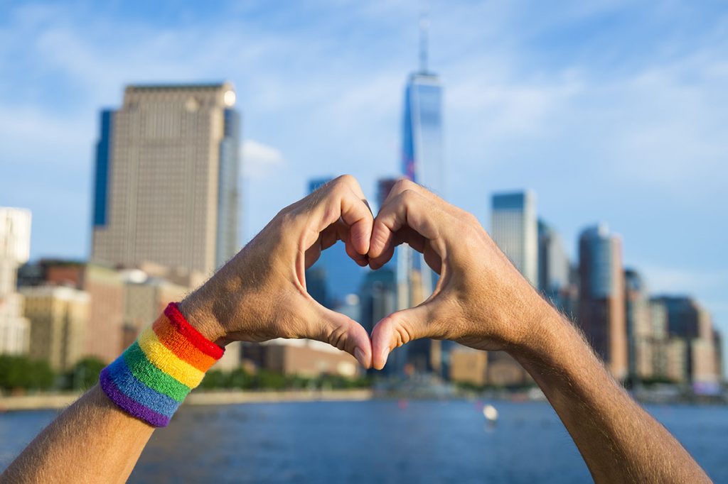 Hands wearing gay pride rainbow sweat band making heart symbol i