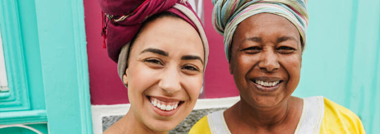 Happy african mother and her daughter wearing afro clothes with a colorful house in background
