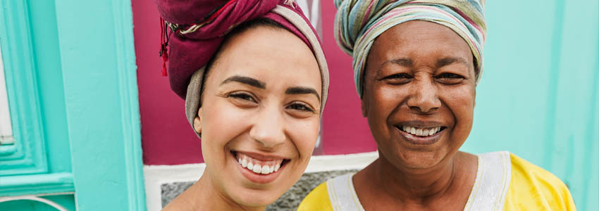 Happy african mother and her daughter wearing afro clothes with a colorful house in background