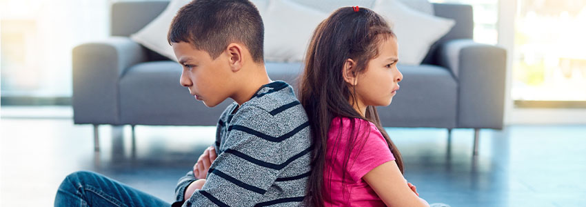 Brother and sister in home living room sitting with arms crossed on floor